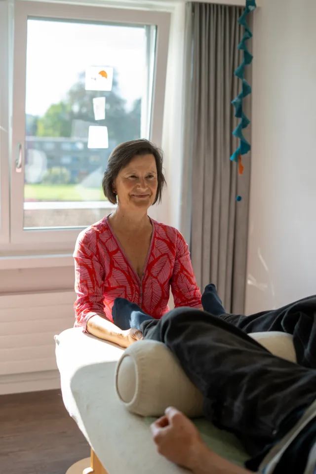 Lisa Kellenberger sitzt am Fussende der Liege, dahinter das helle Fenster