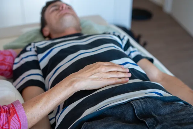 Eine Hand liegt ruhig auf dem Bauch eines entspannt liegenden Mannes